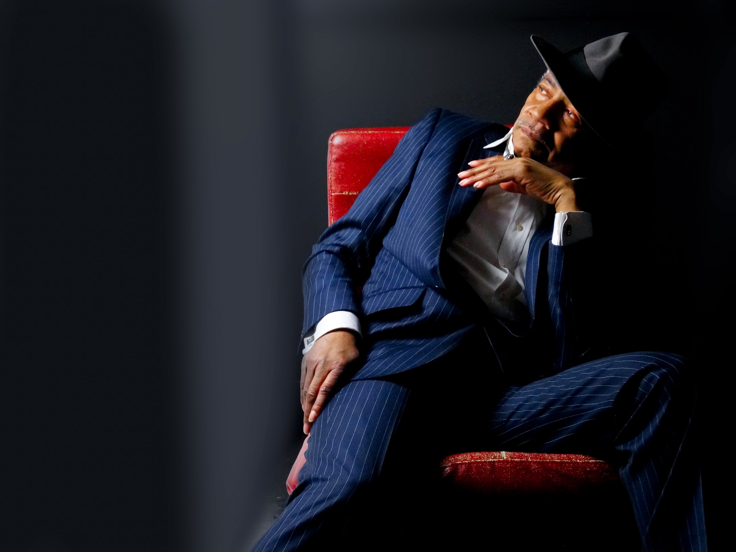 Melvin Moy seated in a blue pinstripe suit and black hat